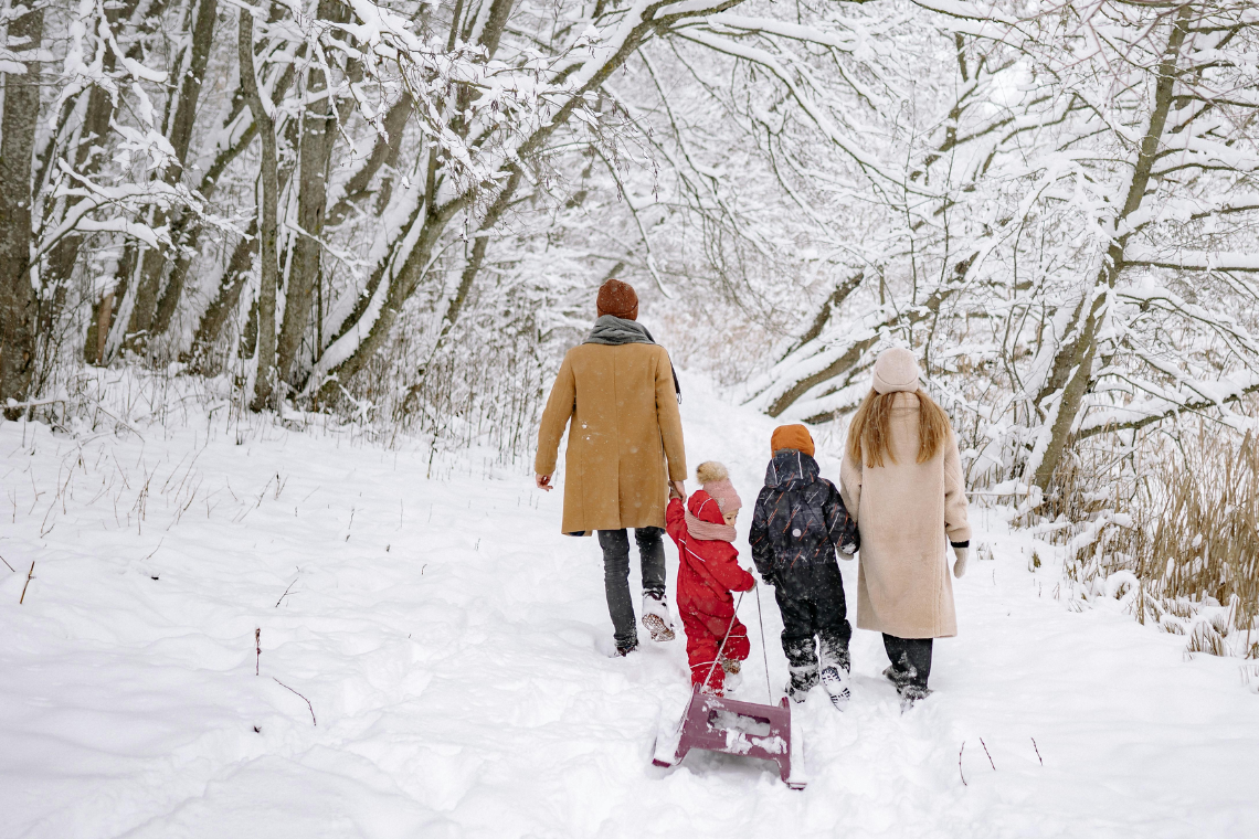 A family of four walks through a snowy path. Their smallest kid is dragging a sled.