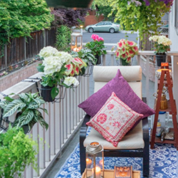 A balcony with a chair with colourful cushions and flowers around