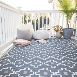 A gray rug lays on a balcony on a sunny day