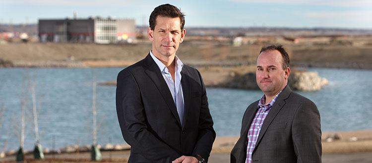 Bordeaux Properties president and CEO Birol Fisekci, left and Qualico Communities senior manager of development Cary Kienitz stand in front of Harmony's central lake, with the community’s water and wastewater treatment facilities pictured in the background. Photo by Wil Andruschak/For CREB®Now