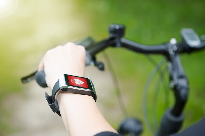 Woman rides her bike with a smartwatch heart rate monitor. 